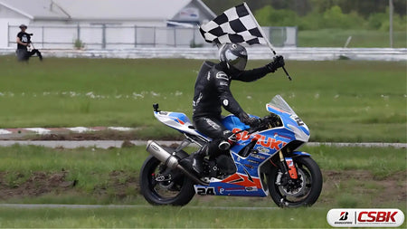 Moto de course bleue et rouge avec un pilote brandissant un drapeau à damiers.