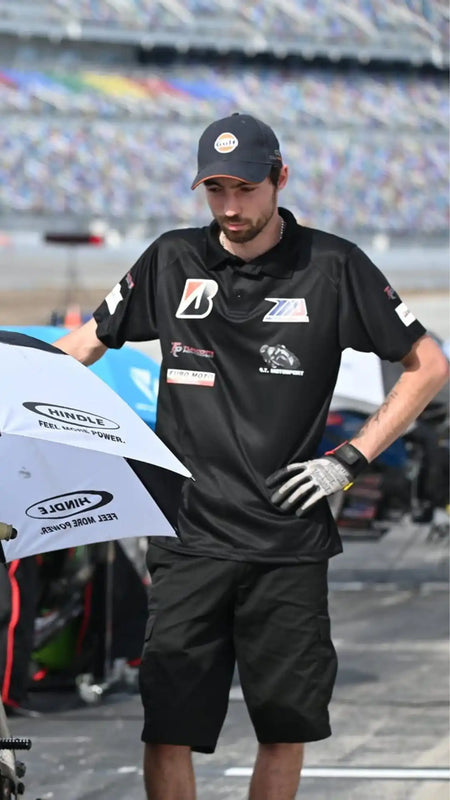 Membre de l'équipe de course portant un uniforme noir et une casquette lors d'un événement de sport automobile.