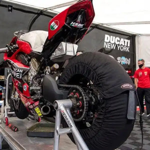 Moto de course Ducati rouge avec des housses de pneus installées sur un support de maintenance.